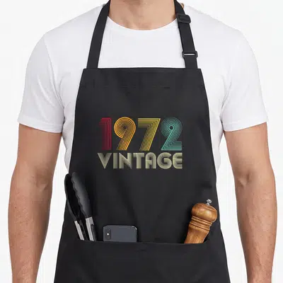Tablier de cuisine noir avec l'inscription 1972 VINTAGE en lettres multicolores à lignes concentriques.