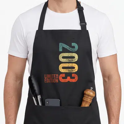 Tablier de cuisine noir avec l'année 2003 en couleurs et le texte Limited Edition imprimé verticalement.
