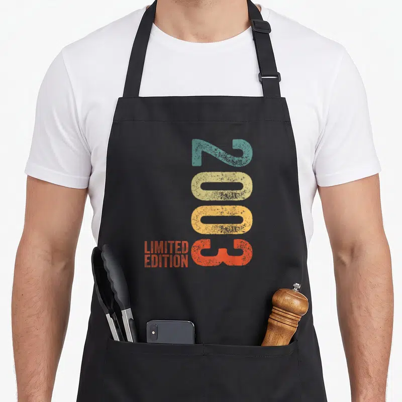 Tablier de cuisine noir avec l'année 2003 en couleurs et le texte Limited Edition imprimé verticalement.