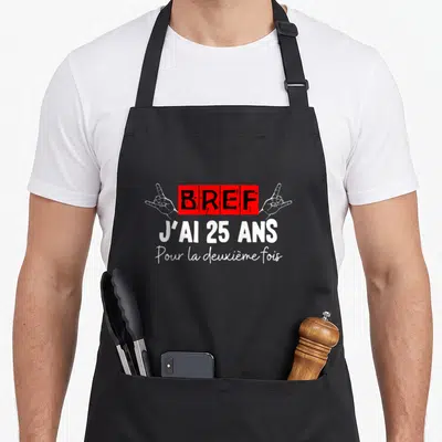 Tablier de cuisine noir avec inscription rouge et blanche « Bref j'ai 25 ans pour la deuxième fois » encadrée par deux mains.