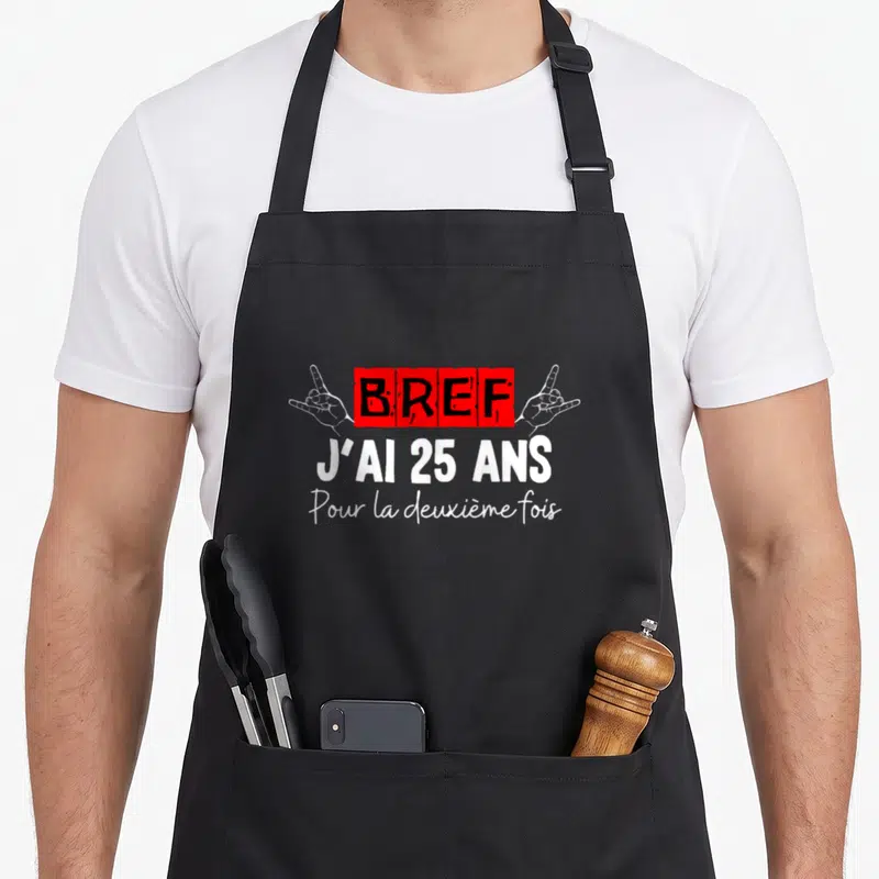 Tablier de cuisine noir avec inscription rouge et blanche « Bref j'ai 25 ans pour la deuxième fois » encadrée par deux mains.
