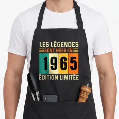 Tablier de cuisine noir avec inscription Les Légendes sont nées en 1965 « Édition Limitée » sur fond coloré vintage.