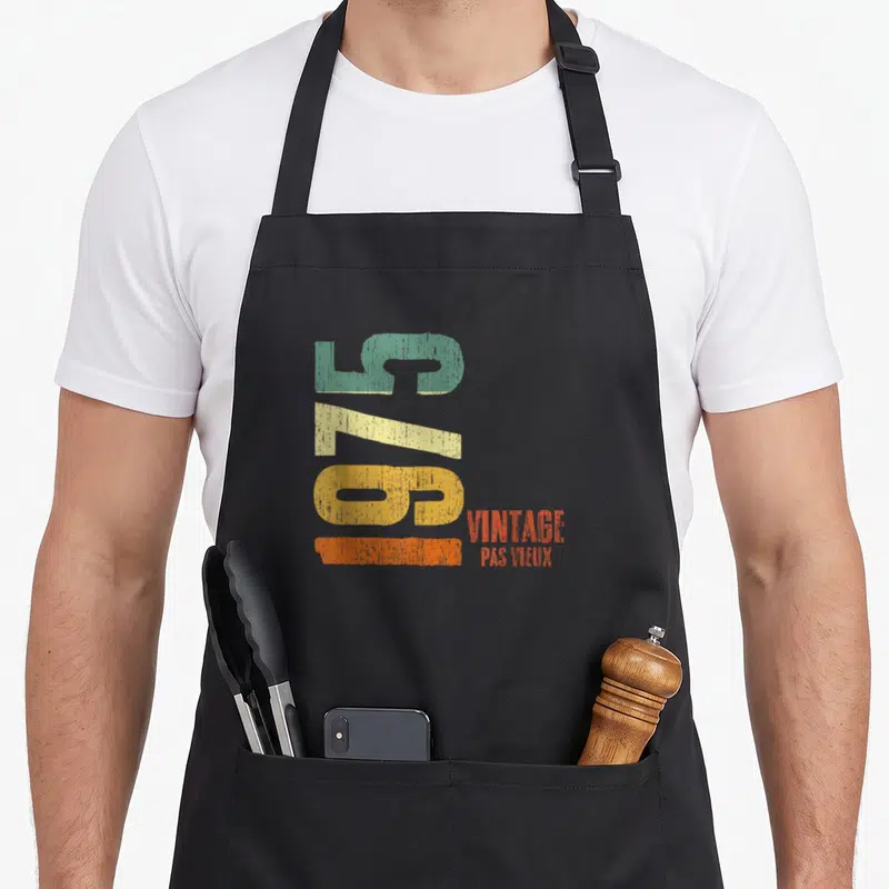 Tablier de cuisine noir avec chiffres 50 vert jaune orange et texte vintage pas vieux imprimé en style rétro.