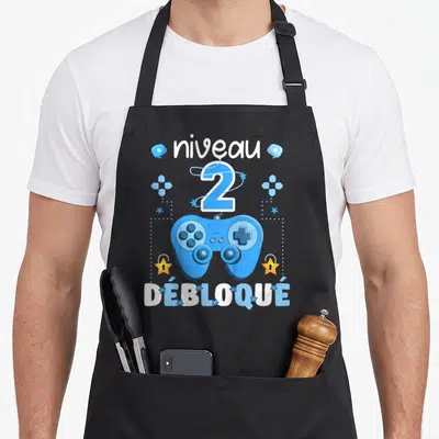 Tablier de cuisine noir avec manette de jeu bleue, niveau 2 débloqué et étoiles dorées.