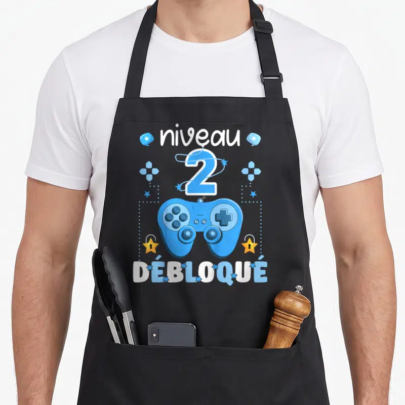 Tablier de cuisine noir avec manette de jeu bleue, niveau 2 débloqué et étoiles dorées.