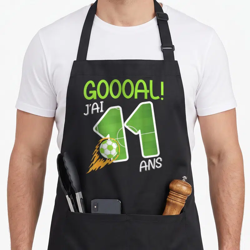 Tablier de cuisine noir avec inscription Gooool J'ai 11 ans et ballon de football enflammé sur fond de terrain vert.
