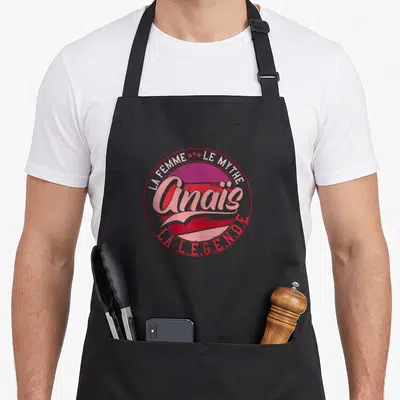Tablier de cuisine noir avec un logo circulaire rose et rouge portant le nom Anais et les mots la femme le mythe la légende.