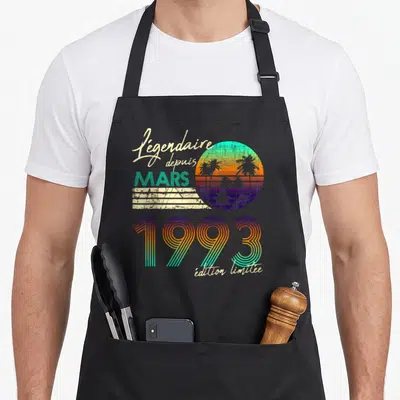 Tablier de cuisine noir avec motif rétro Soleil couchant palmiers et texte Légendaire depuis Mars 1993.