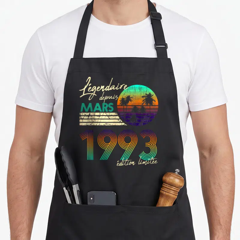 Tablier de cuisine noir avec motif rétro Soleil couchant palmiers et texte Légendaire depuis Mars 1993.
