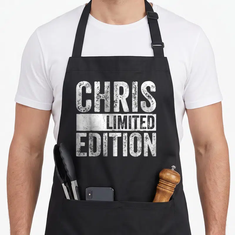 Tablier de cuisine noir avec inscription blanche usée CHRIS LIMITED EDITION centrée sur le devant.