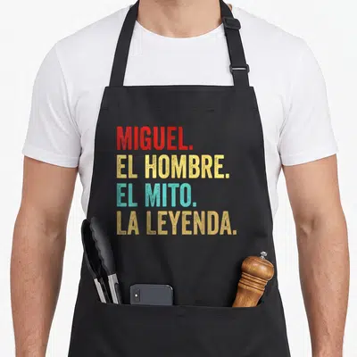 Tablier de cuisine noir avec le texte Miguel El Hombre El Mito La Leyenda en lettres rouges, jaunes et bleues.