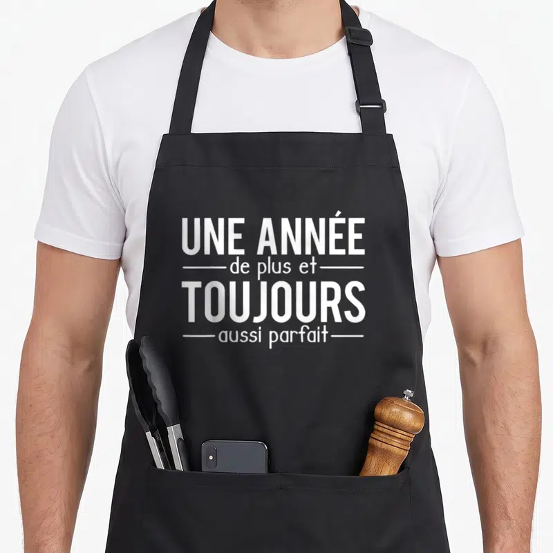 Tablier de cuisine noir avec inscription blanche Une Année De Plus Et Toujours Aussi Parfait centrée sur le devant.