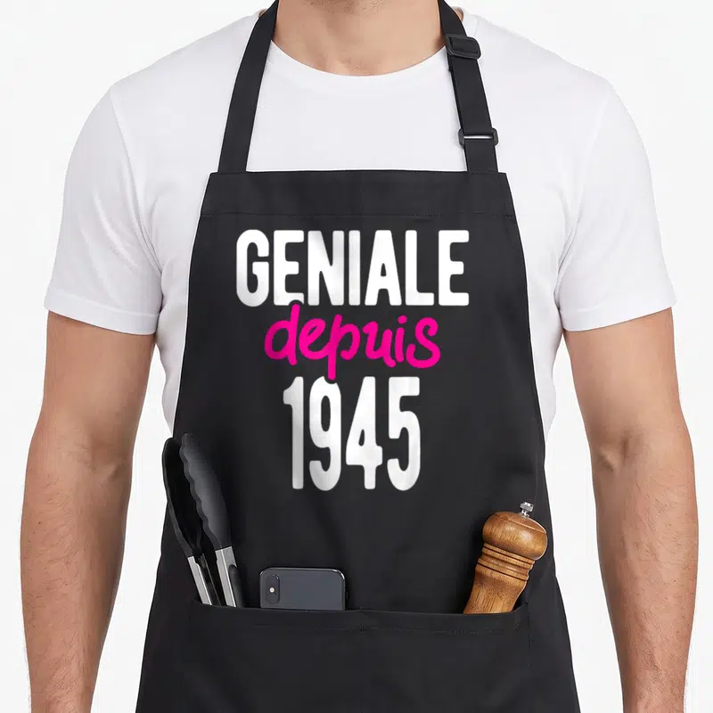 Tablier de cuisine noir avec inscription Géniale depuis 1945 en blanc et rose vif.
