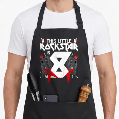 Tablier de cuisine noir avec guitares rouges, enceintes et texte This Little Rockstar is 8 en blanc.