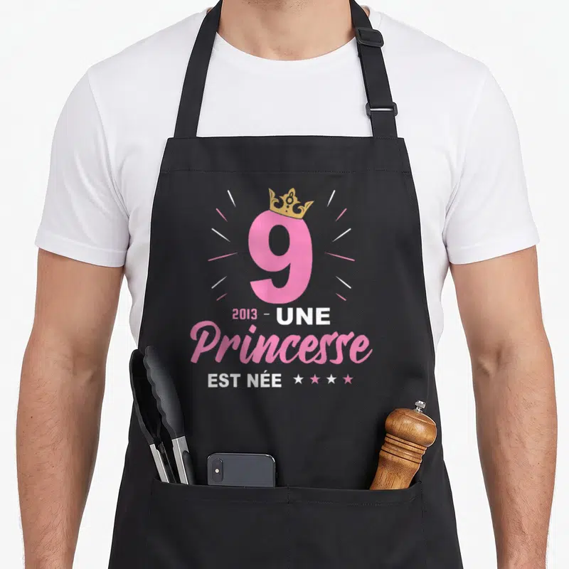 Tablier de cuisine noir avec le chiffre 9 rose, une couronne dorée et le texte Une Princesse Est Née 2013.