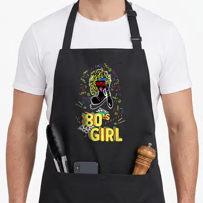 Tablier de cuisine noir avec illustration rétro 80's Girl et lettrage coloré des années 80.