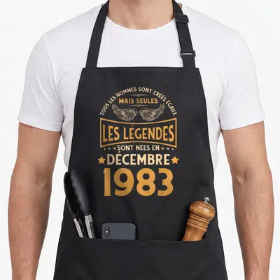 Tablier de cuisine noir avec inscription Les Légendes Sont Nées en Décembre 1983 et motif d'ailes dorées.