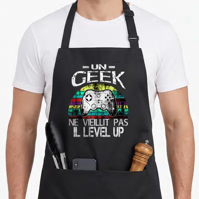Tablier de cuisine noir avec illustration vintage manette de jeu vidéo et texte Un geek ne vieillit pas il level-up.