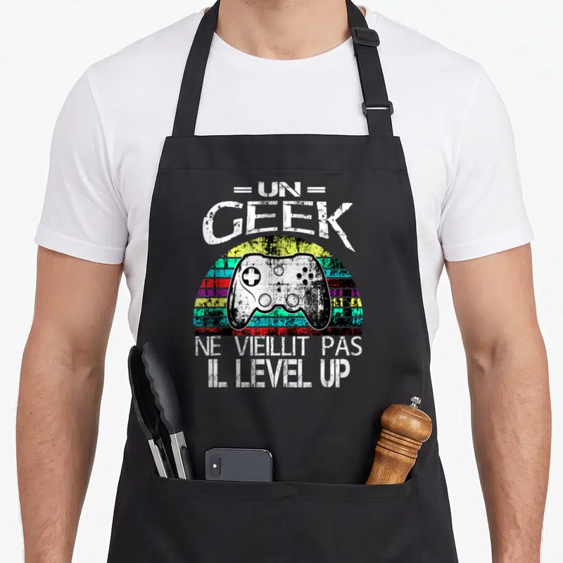 Tablier de cuisine noir avec illustration vintage manette de jeu vidéo et texte Un geek ne vieillit pas il level-up.