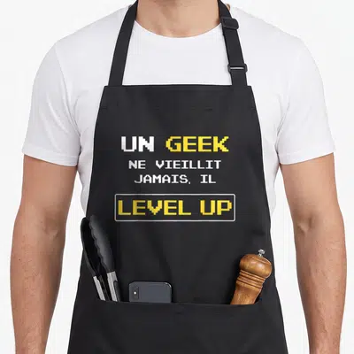 Tablier de cuisine noir avec texte pixel art Un geek ne vieillit jamais level up en jaune et blanc.