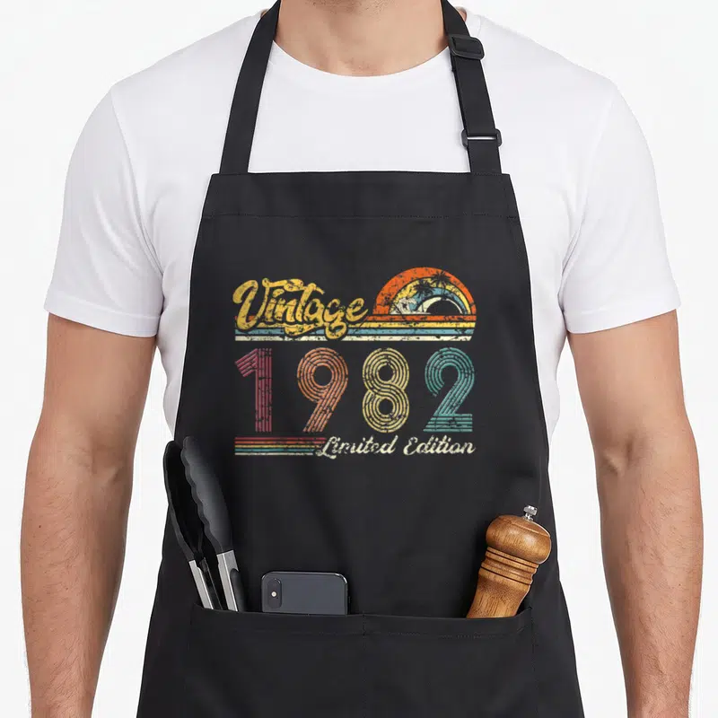 Tablier de cuisine noir avec motif vintage 1982 « édition Limitée » et soleil rétro orange.