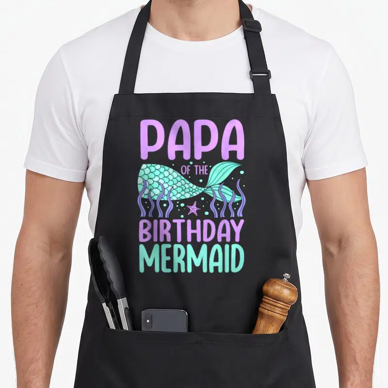 Tablier de cuisine noir avec illustration de queue de sirène turquoise et texte Papa of the anniversaire Mermaid en violet.