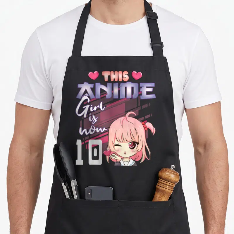 Tablier de cuisine noir avec une illustration d'une fille anime aux cheveux roses et le texte This Anime Girl is now 10