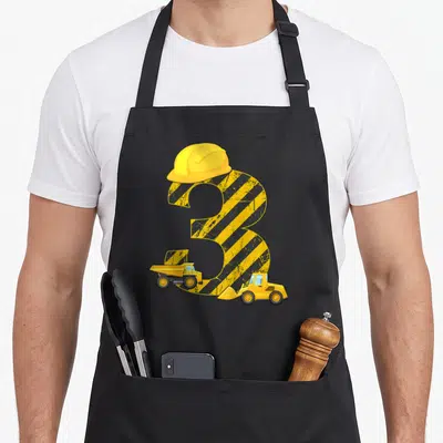 Tablier de cuisine noir avec grand chiffre 3 jaune, casque de chantier, bandes de sécurité et deux engins de construction imprimés.