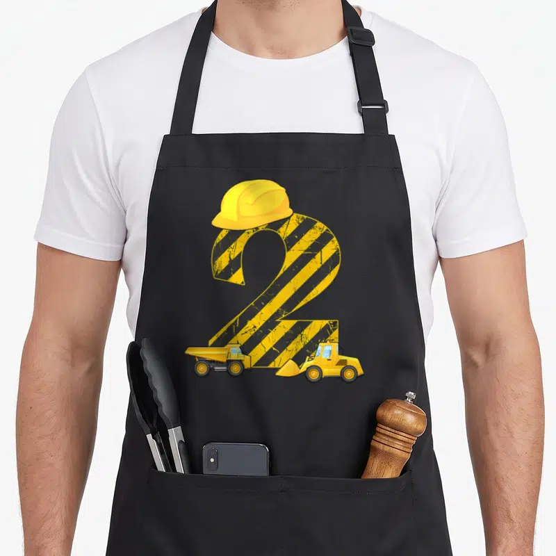 Tablier de cuisine noir avec un chiffre 2 jaune en bandes de chantier, un casque et deux engins de construction.