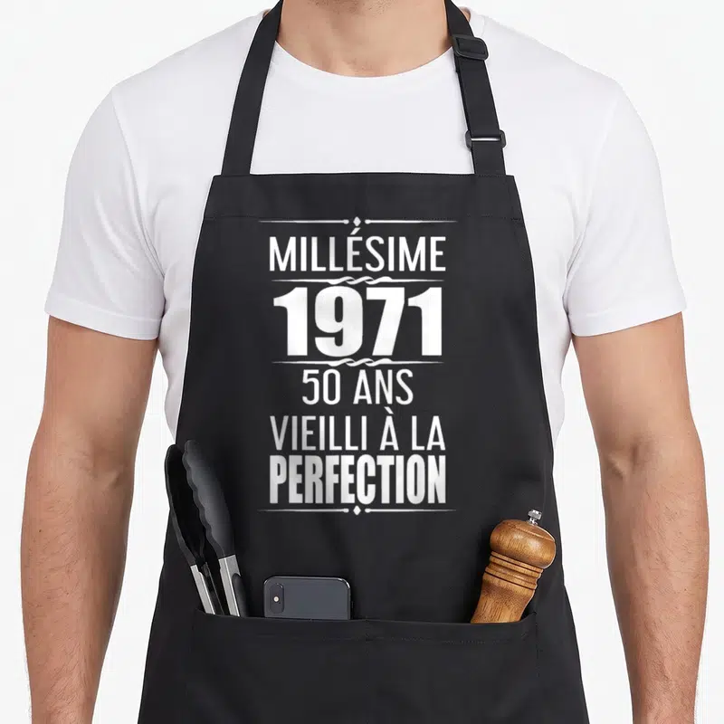 Tablier de cuisine noir avec inscription blanche Millésime 1971 50 ans vieilli à la perfection encadré par des lignes décoratives.