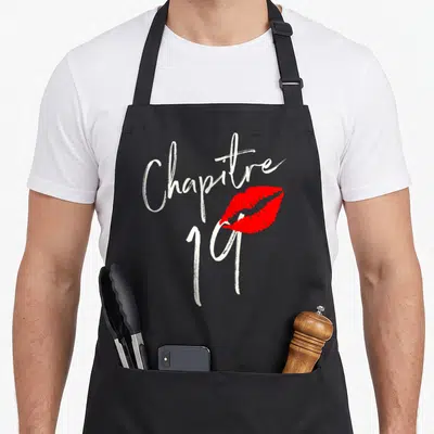 Tablier de cuisine noir avec inscription Chapitre 19 et trace de baisers rouge vif au centre.