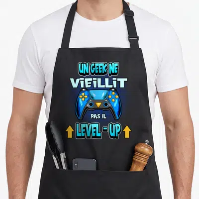 Tablier de cuisine noir avec manette de jeu bleue et texte Un Geek Ne Vieillit Pas Il Level Up.