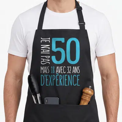 Tablier de cuisine noir avec l'inscription Je n'ai pas 50 ans mais 18 avec 32 ans d'expérience en bleu et blanc.
