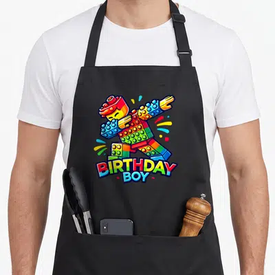 Tablier de cuisine noir avec une figurine de briques multicolores en train de faire le dab au-dessus du texte anniversaire Boy.