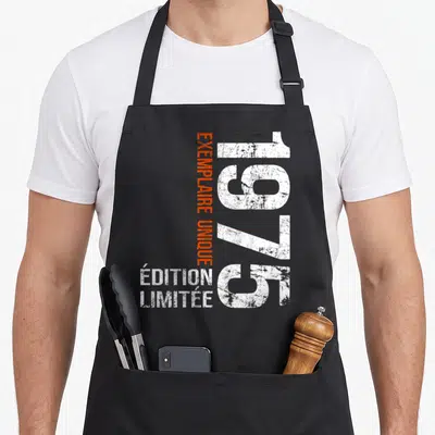 Tablier de cuisine noir avec l'année 1975 en blanc et texte exemplaire unique en orange vertical.