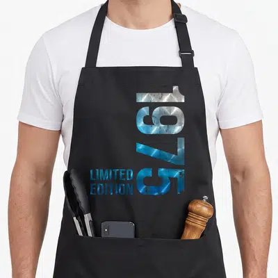 Tablier de cuisine noir avec l'année 1975 en chiffres métalliques bleus et limited edition imprimé verticalement.