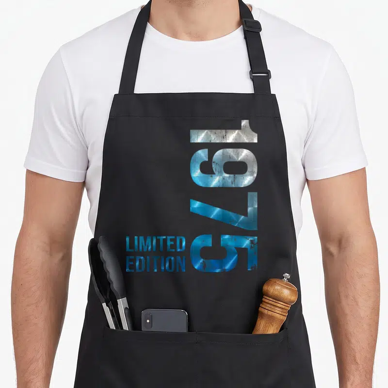 Tablier de cuisine noir avec l'année 1975 en chiffres métalliques bleus et limited edition imprimé verticalement.