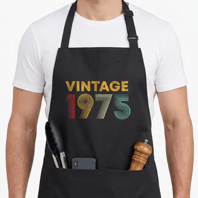 Tablier de cuisine noir avec inscription Vintage 1975 aux couleurs rétro orange, rouge, blanc et turquoise.