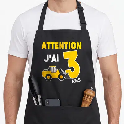 Tablier de cuisine noir avec illustration de pelle jaune et texte Attention j'ai 3 ans imprimé en jaune et blanc.