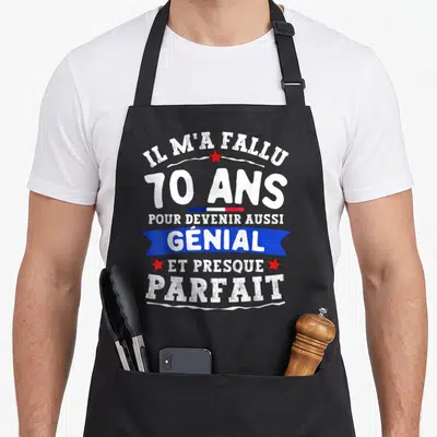 Tablier de cuisine noir avec inscription blanche 70 ans génial et presque parfait sur fond bleu et étoiles rouges.