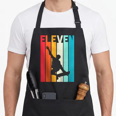Tablier de cuisine noir avec silhouette de skateur et mot ELEVEN sur bandes colorées verticales.