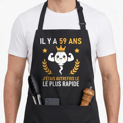 Tablier de cuisine noir avec illustration d'un spermatozoïde souriant couronné et texte sur 59 ans