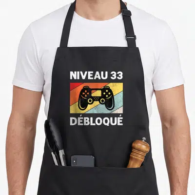Tablier de cuisine noir avec illustration manette de jeu et texte Niveau 33 Débloqué sur bandes colorées vintage.