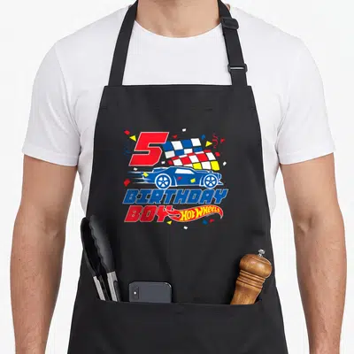 Tablier de cuisine noir avec un numéro 5 rouge, une course bleue Hot Wheels et des confettis colorés.