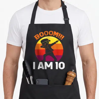 Tablier de cuisine noir avec un personnage effectuant le dab devant un soleil coloré et le texte I AM 10.
