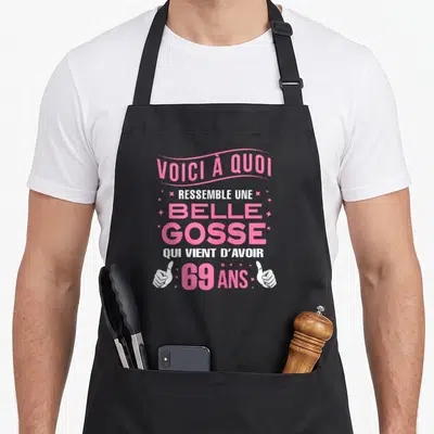 Tablier de cuisine noir avec inscription voici à quoi ressemble une belle gosse qui vient d'avoir 69 ans en rose et blanc.