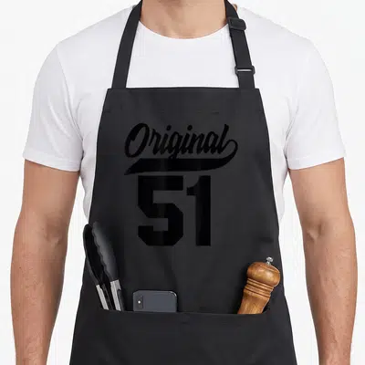 Tablier de cuisine noir avec le mot Original en calligraphie au-dessus du chiffre 51 en gras.