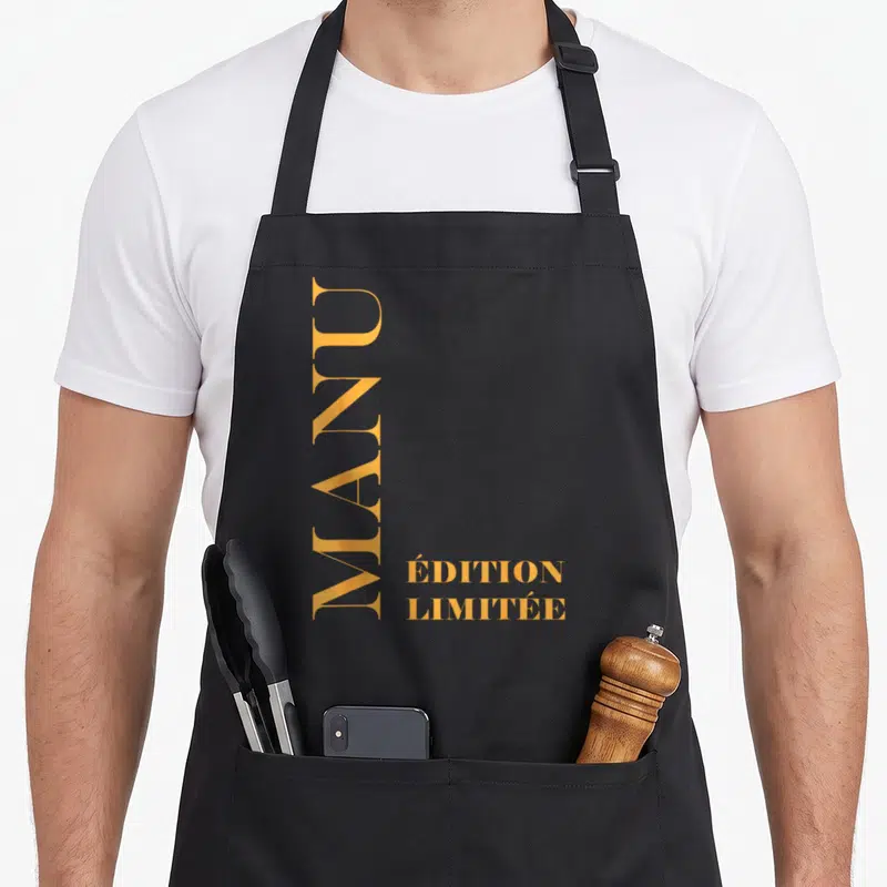 Tablier de cuisine noir avec le prénom Manu et « Édition Limitée » en lettres dorées verticales.