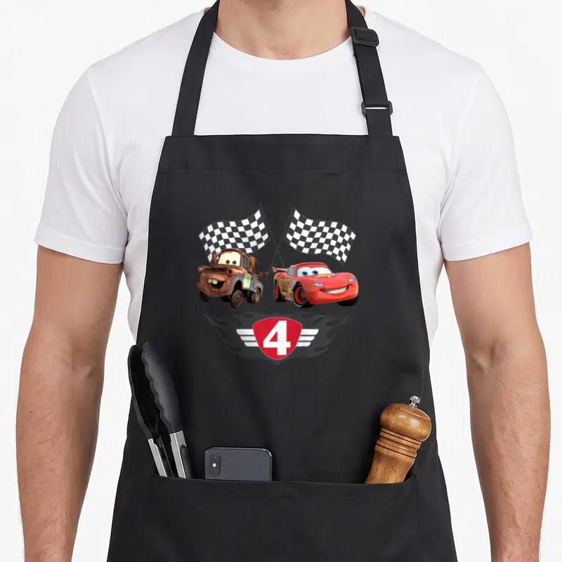 Tablier de cuisine noir avec Lightning McQueen, Mater, drapeaux à damier et le chiffre 4 sur écu.