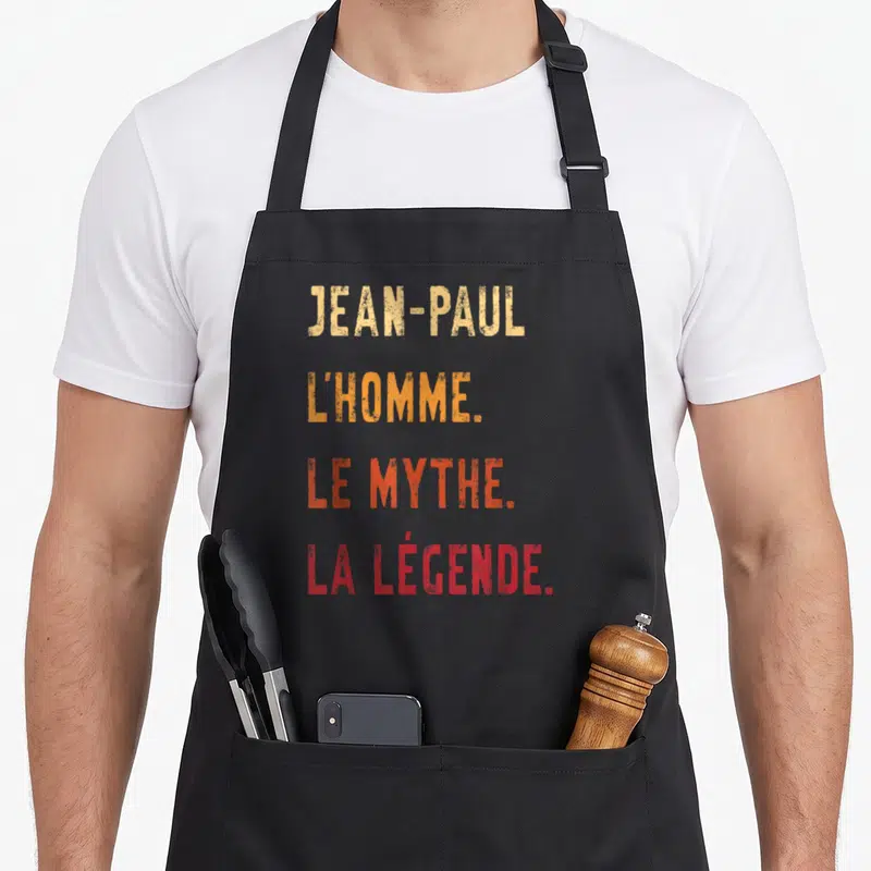 Tablier de cuisine noir avec inscription colorée Jean-Paul L'Homme Le Mythe La Légende en typographie dégradée.